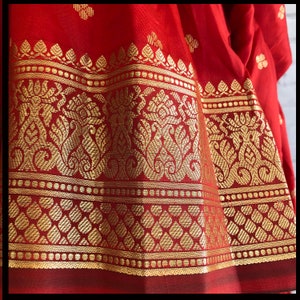 May include: Red silk fabric with a gold border featuring intricate floral patterns. The border has a repeating design of small gold dots.