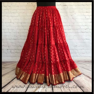May include: A red tiered skirt with gold accents. The skirt has a pattern of small gold squares on a red background. The skirt is made of a soft, flowing fabric and has a wide waistband.