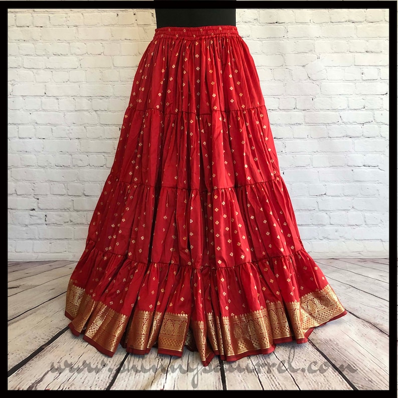 May include: A red tiered skirt with gold accents. The skirt has a pattern of small gold squares on a red background. The skirt is made of a soft, flowing fabric and has a wide waistband.