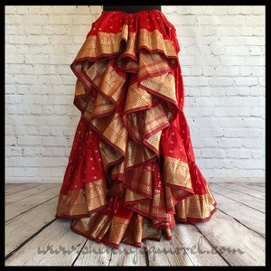 May include: A red and gold layered skirt with multiple ruffles. The skirt is made from a patterned fabric with gold trim.