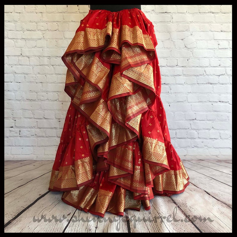 May include: A red and gold layered skirt with multiple ruffles. The skirt is made from a patterned fabric with gold trim.