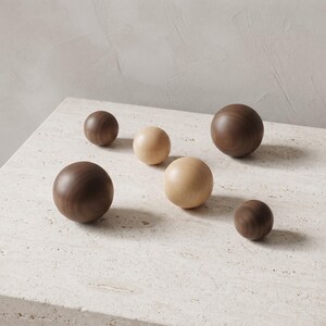 May include: A collection of six smooth, spherical wooden objects of varying sizes. Three spheres are crafted from a dark brown wood, while the other three are made from a lighter, pale beige wood. Each sphere features a visible natural wood grain.