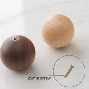 May include: Two spherical wooden knobs, one in a light natural wood tone and one in a dark brown wood tone, each featuring a central metal threaded insert. A single 25mm screw is displayed separately with a line pointing to it for scale.