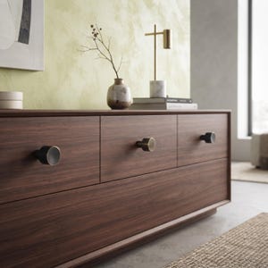 May include: A dark wood dresser featuring three horizontal drawers, each equipped with a single circular knob. The knobs are finished in a metallic tone, providing a contrast against the horizontal wood grain of the drawer fronts.