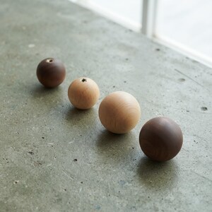 May include: Four spherical wooden knobs arranged in a diagonal line. Two knobs are dark brown, and two are light tan. Each knob features a smooth, rounded surface and a small circular opening at the top, showcasing the natural wood grain texture.