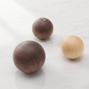 May include: Three spherical wooden knobs with smooth surfaces. Two knobs are dark brown with visible wood grain, and one knob is light beige. Each sphere features a small circular metal threaded insert at the top for mounting purposes.