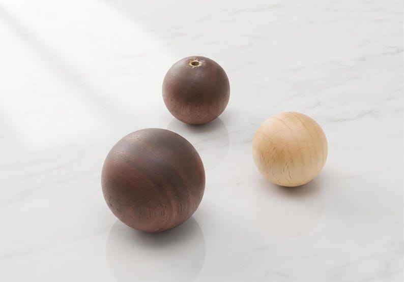 May include: Three spherical wooden knobs with smooth surfaces. Two knobs are dark brown with visible wood grain, and one knob is light beige. Each sphere features a small circular metal threaded insert at the top for mounting purposes.