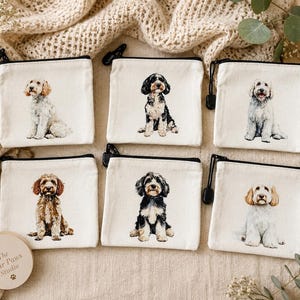 May include: Six rectangular off-white canvas zip pouches, each featuring a unique watercolour-style illustration of a dog sitting. The pouches have black zips with black pulls and are arranged in two rows of three on a textured fabric surface.