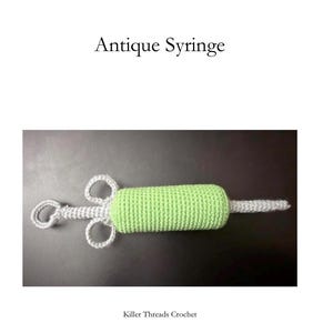 May include: A crochet syringe featuring a light green cylindrical body and a light gray plunger mechanism with two circular finger grips. The text "Antique Syringe" appears above the object, and "Killer Threads Crochet" is printed below.