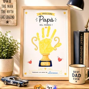 Peut inclure: Une affiche verticale encadrée représentant une empreinte de main jaune en forme de coupe de trophée. Le texte indique IL MIGLIORE Papà DEL MONDO! et N°1 sur la base du trophée. En bas, il est écrit Realizzato con amore da: Lorenzo.