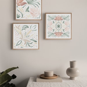 May include: Three framed watercolor paintings with floral designs in shades of pink, green, and yellow. The paintings are hung on a light gray wall.