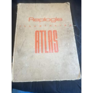 May include: A vintage Replogle Illustrated Atlas with a worn, off-white cover. The title "ATLAS" is prominently displayed in large, orange block letters, with the brand name above. The book shows signs of age and use.