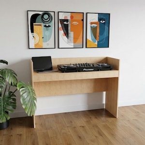 Puede incluir: Un mueble de DJ de madera clara con una mesa de mezclas Pioneer y un portátil. Tres obras de arte abstractas enmarcadas cuelgan sobre el mueble. Una gran planta en maceta y un altavoz negro están a la izquierda.