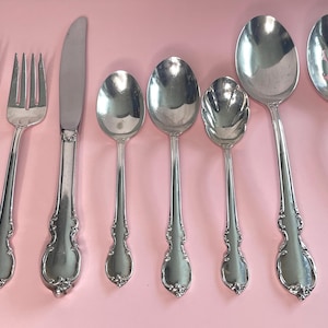 Könnte beinhalten: Ein Set aus acht silberfarbenen Edelstahlbesteckteilen, die in einer Reihe angeordnet sind, darunter zwei Gabeln, ein Tafelmesser, drei Löffel unterschiedlicher Größe, ein großer Servierlöffel und ein großer geschlitzter Servierlöffel.