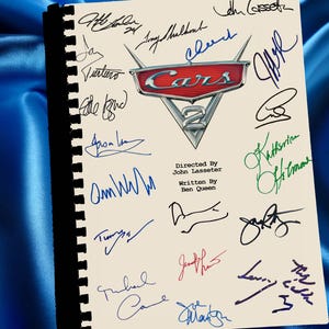 Peut inclure: Un cahier à spirales avec le logo "Cars 2" et de nombreuses signatures de différentes couleurs. Le logo est rouge, argenté et blanc. Le texte sur la page indique "Réalisé par John Lasseter" et "Écrit par Ben Queen".