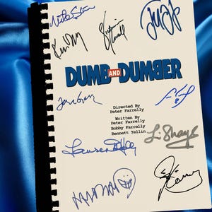 May include: A cream-colored script with the title "Dumb and Dumber" in blue and red, surrounded by multiple signatures in blue and black ink. The script is bound with a black spine and rests on a blue satin surface.