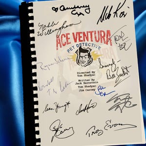Puede incluir: Un guion de "Ace Ventura: Pet Detective" con múltiples firmas. El título es rojo, con una imagen de dibujos animados de Ace Ventura. El guion está encuadernado con una espina negra y descansa sobre una superficie de satén azul.
