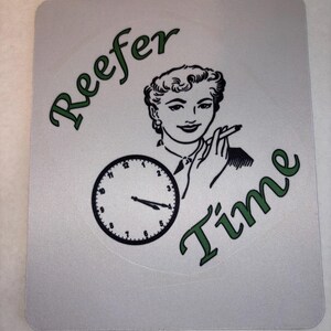 May include: A square light gray mousepad featuring a black and white illustration of a person holding a cigarette. Below the person is a black clock face with hands set to approximately 4:20. The text "Reefer Time" is printed in dark green.