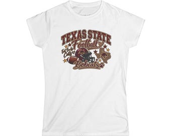 May include: A white short-sleeved t-shirt featuring a maroon and gold graphic design that reads Texas State Football Bobcats and Eat Em Up Cats. The design includes a football, a helmet, a state of Texas outline, stars, and a paw print.