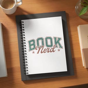 May include: A white spiral notebook with the words "BOOK Nerd" in teal and brown, with star accents. The notebook is on a black surface, with a cup of coffee and books in the background.