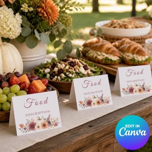 May include: Three white folded cardstock food labels with the text Food DESCRIPTION and a colorful autumn floral illustration at the bottom. The cards are arranged on a wooden table alongside bowls of fresh fruit, salad, and croissant sandwiches.