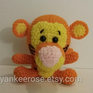 May include: A crocheted stuffed toy of Tigger from Winnie the Pooh. The toy is orange and yellow with black eyes and a pink nose.