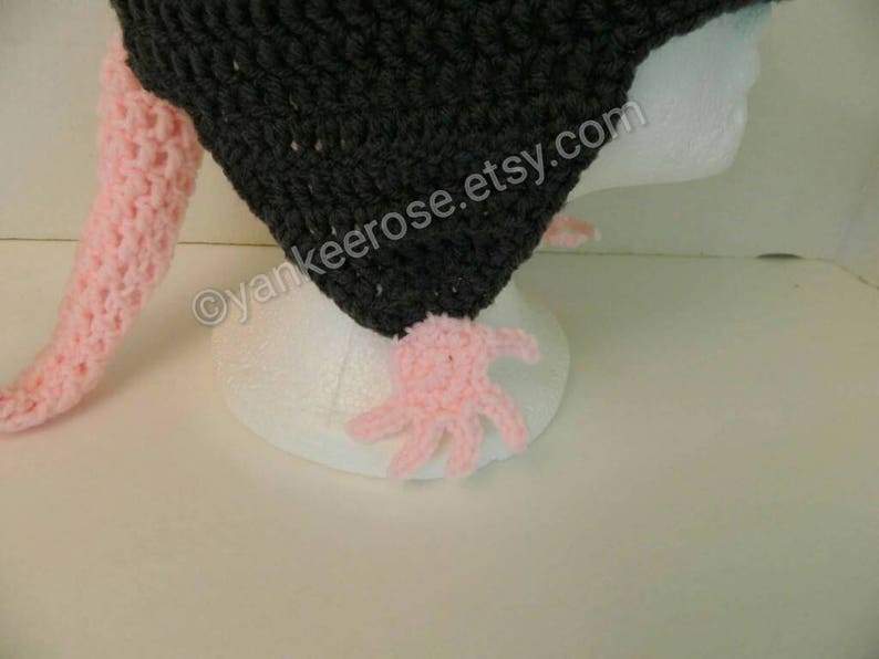 May include: A black crocheted hat with a pink crocheted tail. The hat is on a white mannequin head. The text "yankeerose.etsy.com" is on the hat.