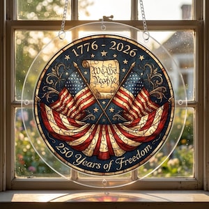 May include: A round, clear glass decoration with a patriotic design. It features two American flags crossed over each other, a scroll with the words "We the People," and the text "1776 - 2026" and "250 Years of Freedom."