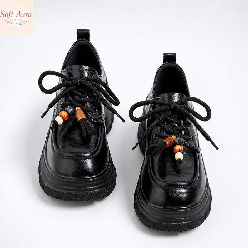 May include: Pair of black leather shoes with thick soles and decorative tassels. The shoes have black laces and are adorned with wooden beads. The shoes are a stylish and unique footwear option.