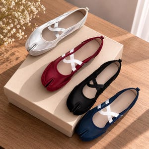 May include: Four split-toe ballet flats featuring a distinctive cleft design at the toe, crisscross straps across the instep, and a low-profile silhouette. The shoes are presented in silver, deep red, black, and navy blue colorways.