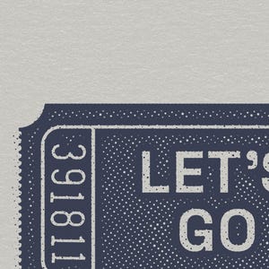 Puede incluir: Un boleto rectangular azul oscuro con un borde perforado, que presenta el texto blanco LET'S GO y el n&uacute;mero vertical 391811. El dise&ntilde;o tiene una textura de semitonos punteada sobre un fondo gris claro, imitando un pase de entrada vintage.