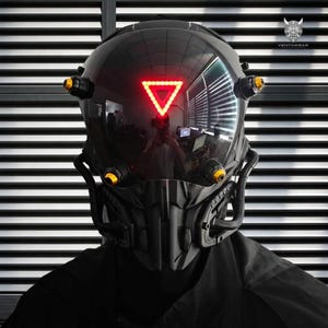 May include: A black full-face helmet featuring a dark reflective visor with a glowing red triangular light in the centre. The helmet includes four gold-toned circular accents and a structured, angular lower face guard with integrated tubing.