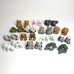 May include: A collection of small ceramic animal figurines including pairs of tigers, pigs, elephants, turtles, dogs, lions, and polar bears. Each miniature figure features hand-painted details, varied textures, and distinct color patterns.