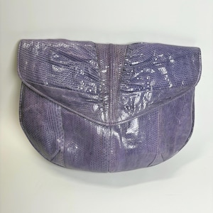 Peut inclure: Une pochette lavande avec un motif texturé semblable à des écailles de reptile. Le sac présente un bord inférieur arrondi et une fermeture à rabat avec des détails froncés et plissés rayonnant depuis une couture centrale verticale.