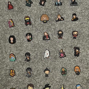 May include: A collection of colorful, cartoon-style charms featuring characters from a popular fantasy series. The charms are arranged on a gray surface and include various characters in different poses and outfits.
