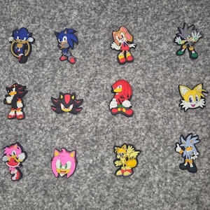 May include: A collection of twelve colourful rubber shoe charms featuring various Sonic the Hedgehog characters including Sonic, Shadow, Knuckles, Tails, Amy Rose, Cream the Rabbit, and Silver the Hedgehog in various poses and facial expressions.
