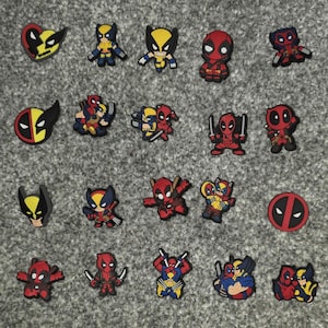 Puede incluir: Una colección de coloridos dijes para zapatos con varios personajes de cómics de Marvel. Los dijes incluyen a Deadpool y Wolverine en diferentes poses y diseños, con combinaciones de colores rojo, amarillo y negro. Los dijes están dispuestos sobre una superficie gris.