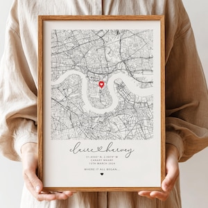 May include: A wooden framed map print showing a detailed black and white city map, with a red heart indicating a location. The print includes the names "Claire & Harvey", coordinates, date, and the phrase "WHERE IT ALL BEGAN..." in elegant script.