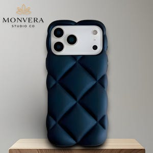 May include: A navy blue quilted phone case with a white camera module. The case has a diamond pattern and is displayed on a wooden block. The logo "MONVERA STUDIO CO" is visible in the background.