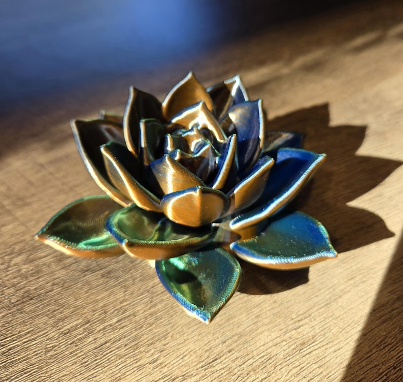 May include: A three-dimensional succulent sculpture featuring layered, pointed petals with a metallic finish that shifts between deep navy blue, emerald green, and bronze gold tones, creating a vibrant, multi-colored appearance.