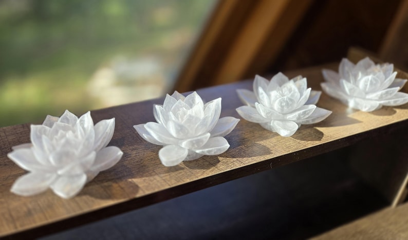 May include: Four white, translucent, carved stone lotus flower sculptures arranged in a row. Each flower features multiple layered, pointed petals radiating from a central point, creating a symmetrical, blooming appearance with a smooth, polished finish.