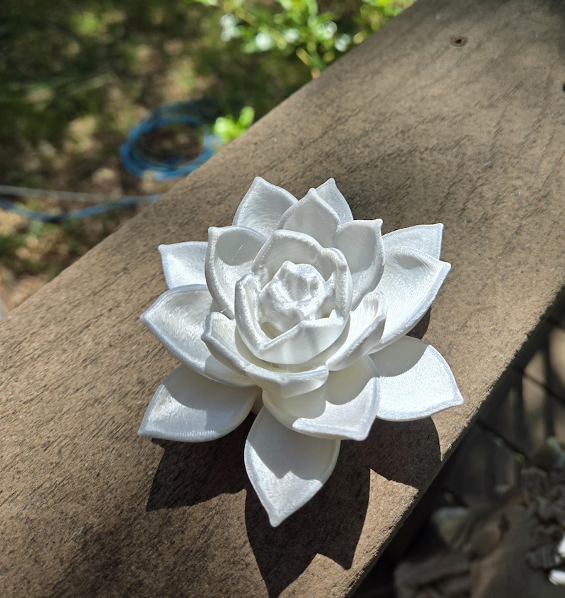 May include: A white, multi-layered succulent plant sculpture with pointed, overlapping petals arranged in a circular, blooming pattern. The object has a smooth, matte finish and a symmetrical structure, showcasing a detailed, realistic botanical form.