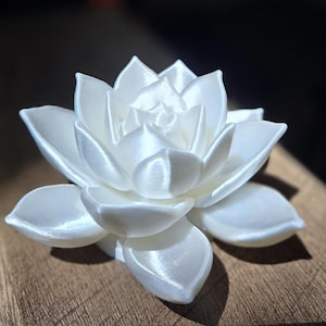 May include: A white, multi-layered lotus flower sculpture with a smooth, satin-like finish. The petals are arranged in a radial pattern, curving outward from the center to create a realistic, blooming appearance with subtle light reflections.