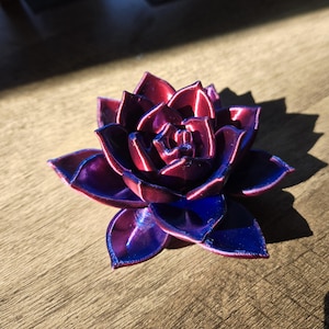 May include: A multi-layered succulent sculpture featuring a vibrant color gradient that shifts from deep magenta at the center to a rich, saturated royal blue at the outer petal tips, showcasing a smooth, reflective, and layered finish.