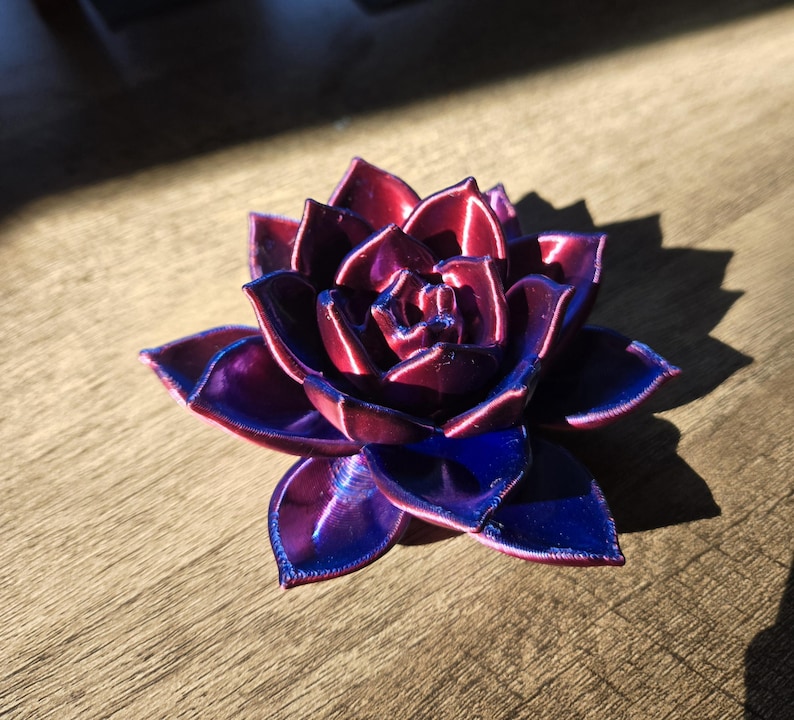 May include: A multi-layered succulent sculpture featuring a vibrant color gradient that shifts from deep magenta at the center to a rich, saturated royal blue at the outer petal tips, showcasing a smooth, reflective, and layered finish.