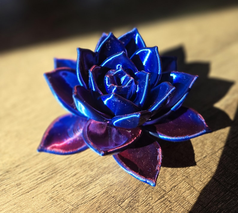 May include: A three-dimensional succulent sculpture featuring layered, pointed petals. The finish is a vibrant, glossy gradient that transitions from a deep, saturated royal blue at the center to a rich, dark purple hue at the outer petal edges.