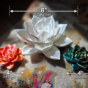 May include: Three succulent-shaped decorative objects. The central white succulent measures 8 inches in diameter. The orange succulent on the left and the dark green succulent on the right each measure 4 inches in diameter.