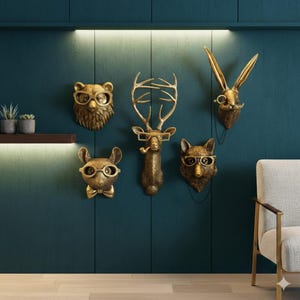 May include: A set of gold-toned animal head wall sculptures, featuring a bear, deer, rabbit, fox, and mouse, each sporting spectacles. The deer holds a pipe. They are mounted on a dark teal wall, offering a quirky and decorative feature.