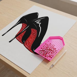 May include: Illustration of black high-heeled shoes with red jeweled soles. A pink tray filled with red rhinestones and a pen are next to the image. The artwork is on a white background.