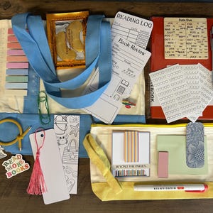 May include: A collection of stationery and reading accessories including a light blue tote bag, a red notebook with a date due card, a yellow pencil case, sticky notes, stickers, bookmarks, a pen, a highlighter, and gold-coloured eye masks.